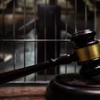 Judge's gavel on wooden block with prison cell bars in background symbolizing law and justice