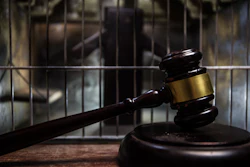 Judge's gavel on wooden block with prison cell bars in background symbolizing law and justice