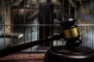 Judge's gavel on wooden block with prison cell bars in background symbolizing law and justice
