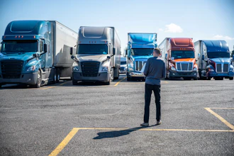 Businessman standing in parking lot facing row of commercial semi-trucks in various colors under clear sky