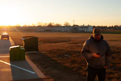 Person standing in rural area at sunset with vehicles and farm buildings in background