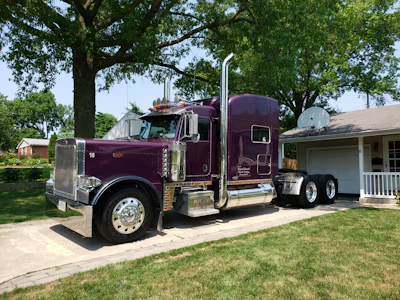 Maroon Peterbilt semi-truck parked in residential driveway with trees and house