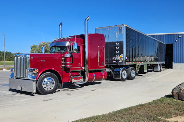 Red Peterbilt semi-truck with custom black enclosed trailer parked in lot