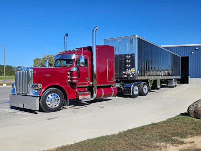 Red Peterbilt semi-truck with custom black enclosed trailer parked in lot