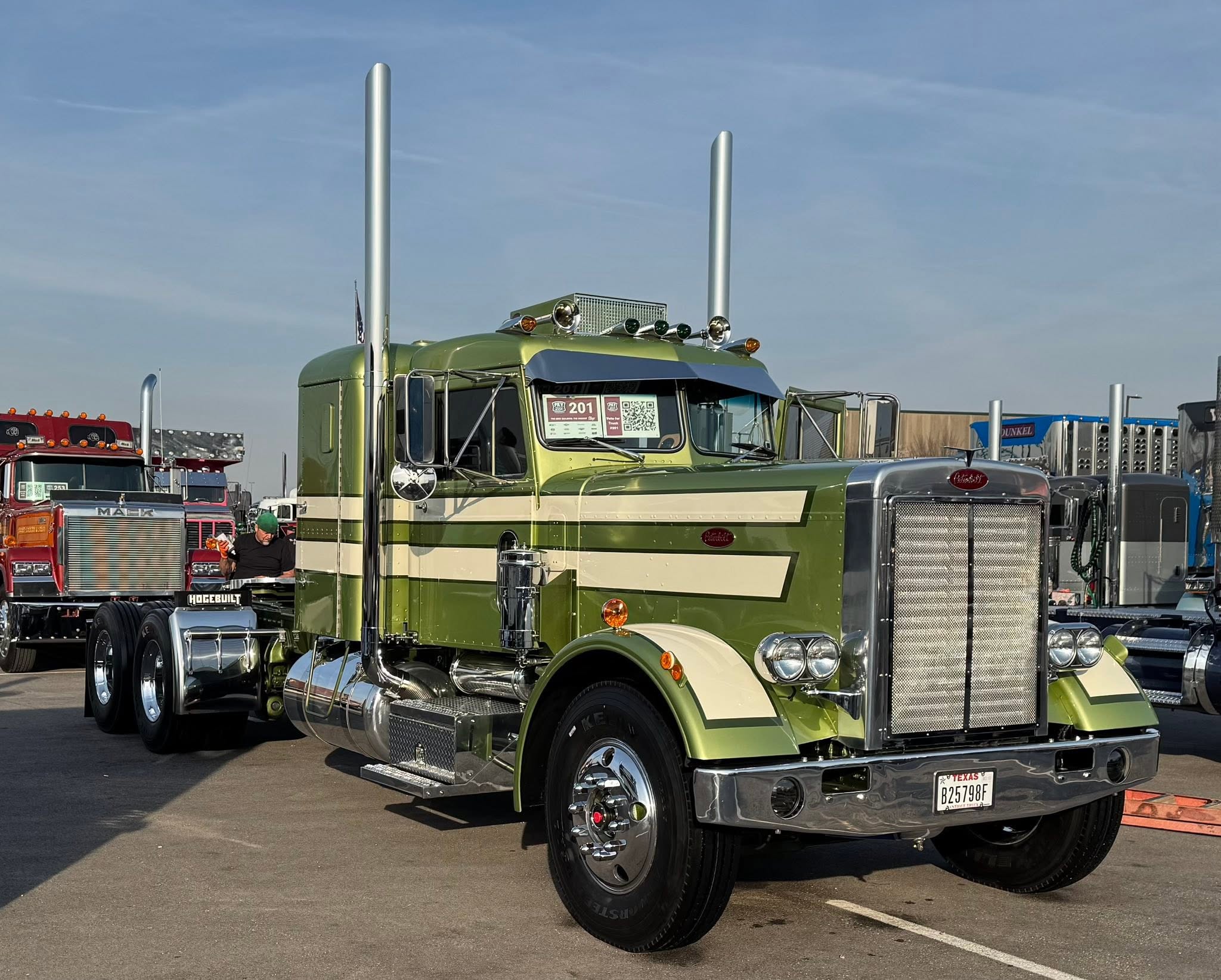 Green and cream Peterbilt semi-truck with dual exhaust stacks displayed at outdoor truck show