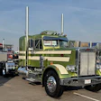 Green and cream Peterbilt semi-truck with dual exhaust stacks displayed at outdoor truck show