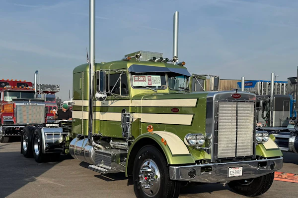 Green and cream Peterbilt semi-truck with dual exhaust stacks displayed at outdoor truck show