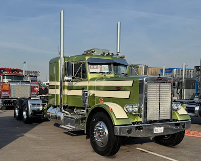 Green and cream Peterbilt semi-truck with dual exhaust stacks displayed at outdoor truck show