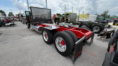 Red and white semi-truck tractor with polished chrome wheels displayed at commercial vehicle show