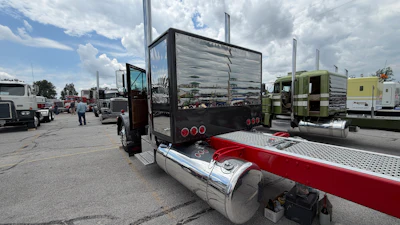 Commercial truck with red and silver trailer parked at busy truck lot with multiple vehicles and cloudy sky