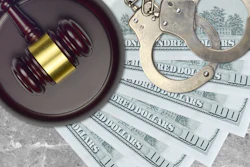 Gavel, handcuffs, and hundred-dollar bills arranged on concrete surface representing law, justice, and financial crime.