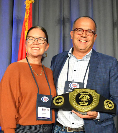 Two smiling people at awards ceremony holding championship belt with gold emblem