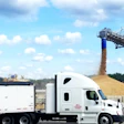 White semi-truck loading grain from industrial conveyor system at agricultural facility