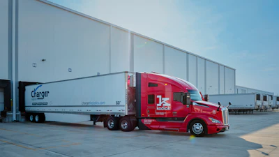 Red Kodiak semi-truck with white Charger refrigerated trailer parked at industrial loading dock