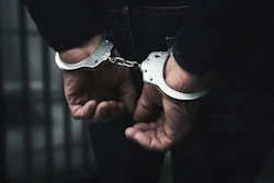 Person wearing handcuffs with hands restrained in dark lighting