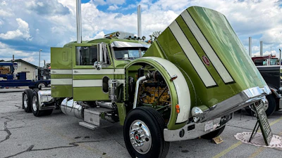 Vintage lime-green and white custom semi-truck with chrome details and tilted cargo bed at outdoor truck show
