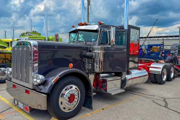 Vintage black semi-truck with chrome details and orange lights displayed at outdoor truck show