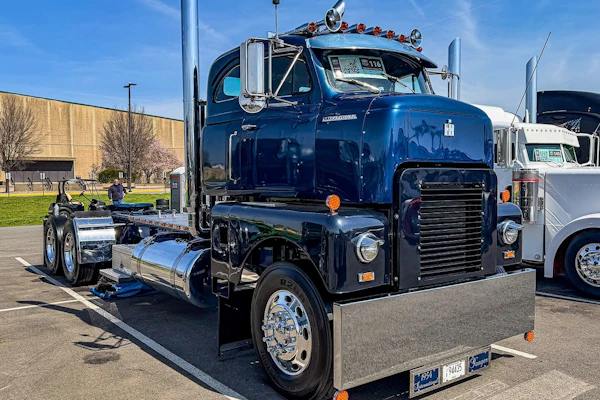 Vintage blue and black semi-truck with polished chrome details displayed at outdoor truck show