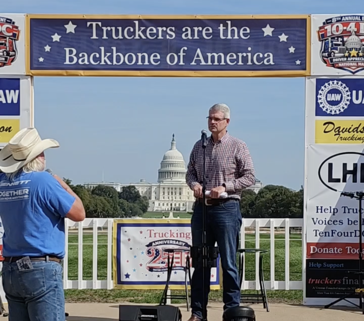 Man speaking at podium during trucking industry rally in front of U.S. Capitol building with industry banners and signage