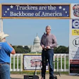 Man speaking at podium during trucking industry rally in front of U.S. Capitol building with industry banners and signage