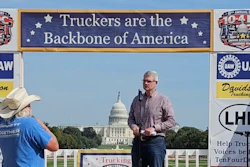 Man speaking at podium during trucking industry rally in front of U.S. Capitol building with industry banners and signage