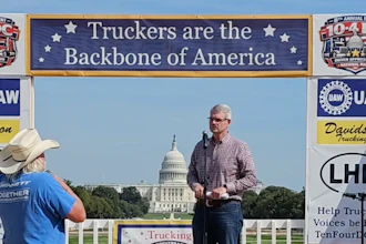Man speaking at podium during trucking industry rally in front of U.S. Capitol building with industry banners and signage