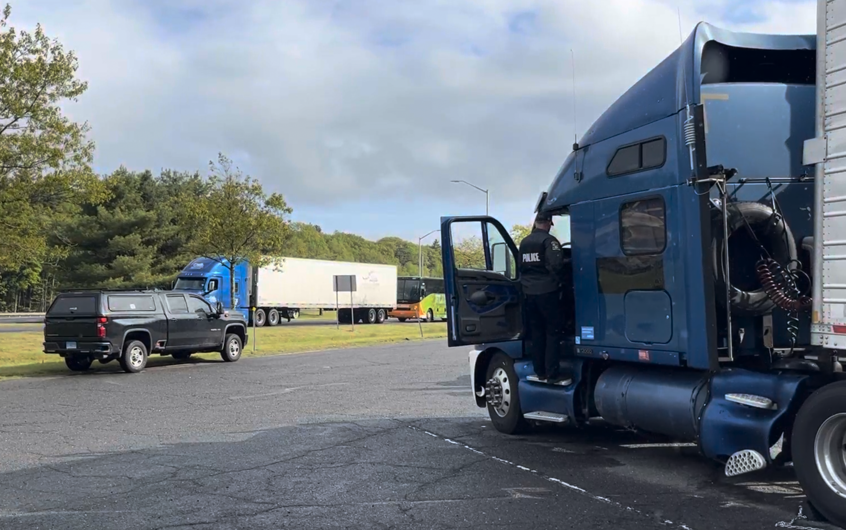 Blue semi-truck with open driver door parked in yard beside pickup truck and trailers