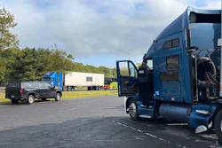 Blue semi-truck with open driver door parked in yard beside pickup truck and trailers
