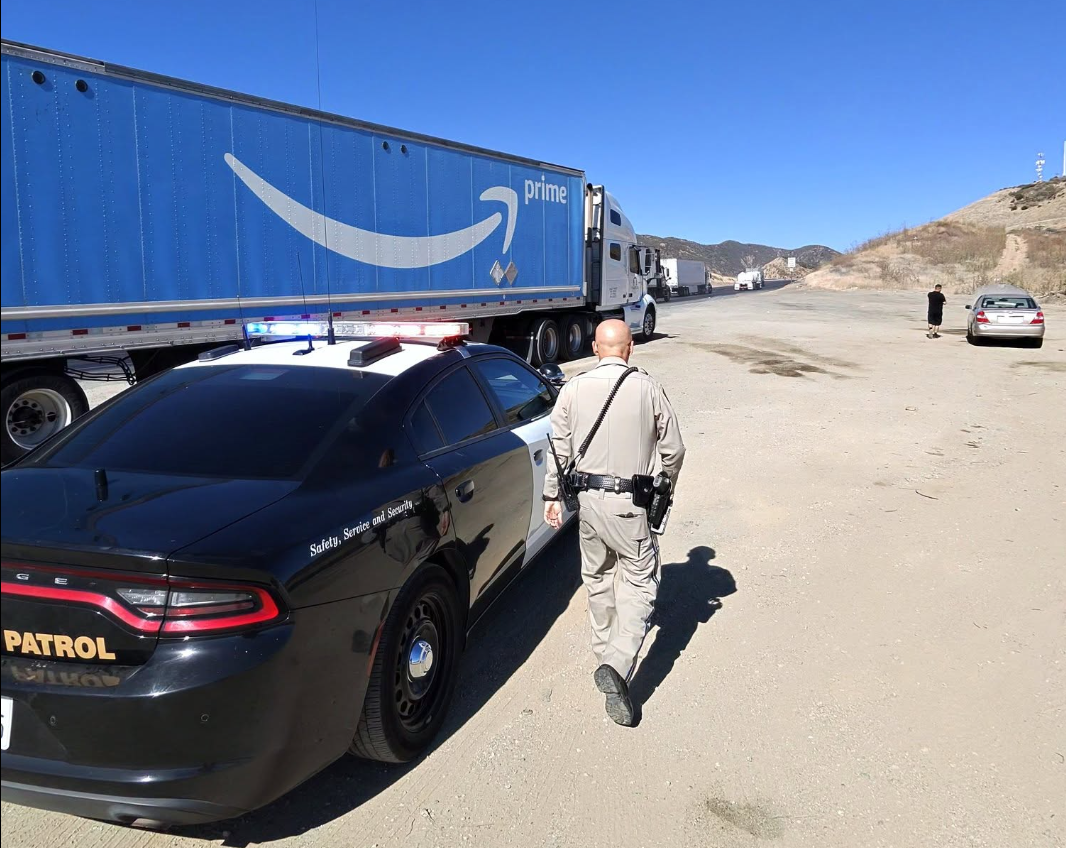 Police officer inspecting Amazon Prime delivery truck on desert highway with vehicles in background