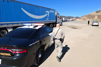 Police officer inspecting Amazon Prime delivery truck on desert highway with vehicles in background