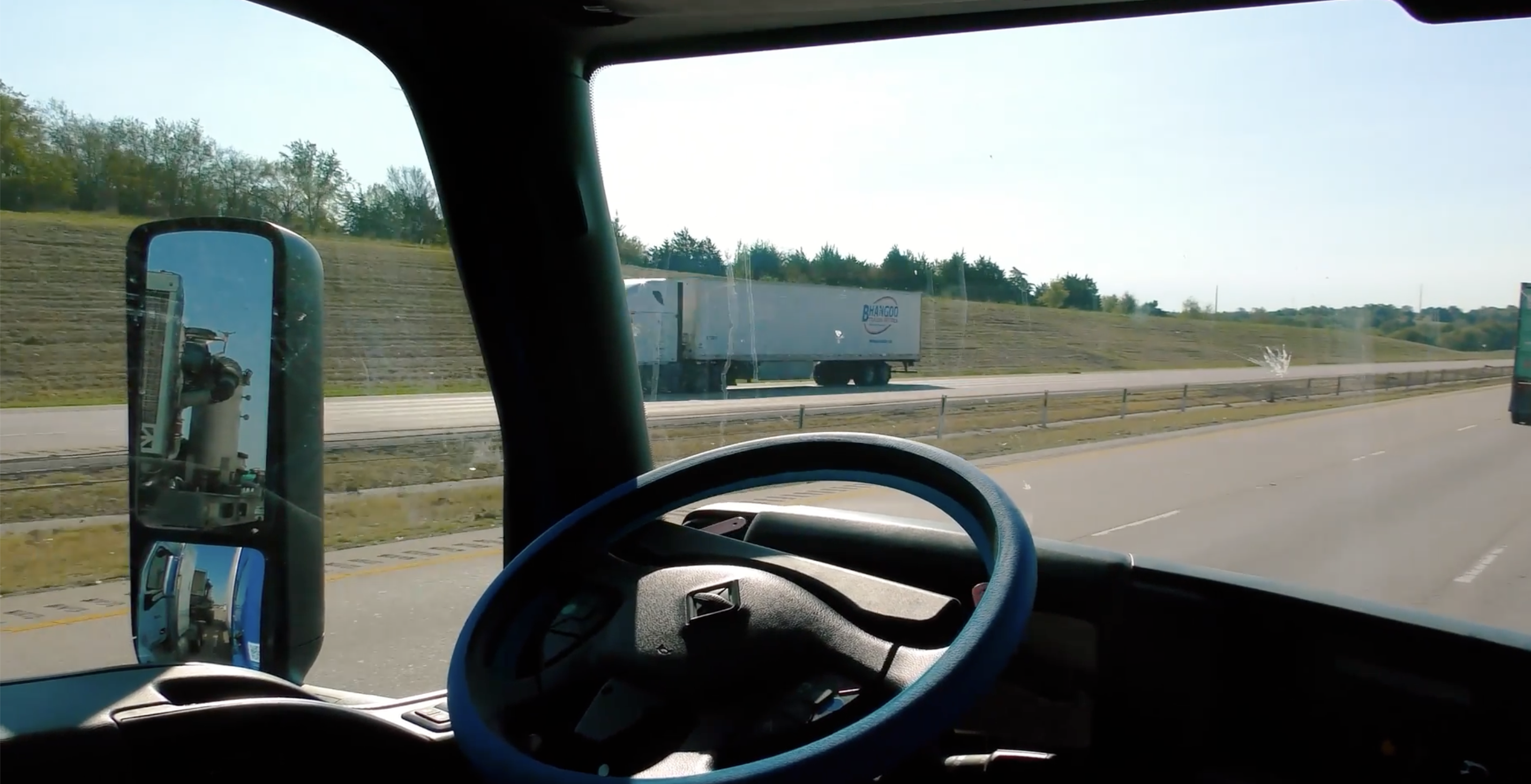 View from truck cab on highway with steering wheel and another truck ahead on the road