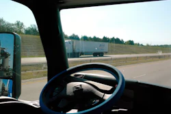 View from truck cab on highway with steering wheel and another truck ahead on the road