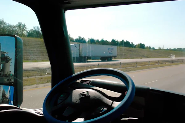 View from truck cab on highway with steering wheel and another truck ahead on the road
