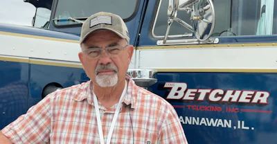 Man in cap and plaid shirt standing in front of Betcher Trucking Inc truck in Hanauan, Illinois