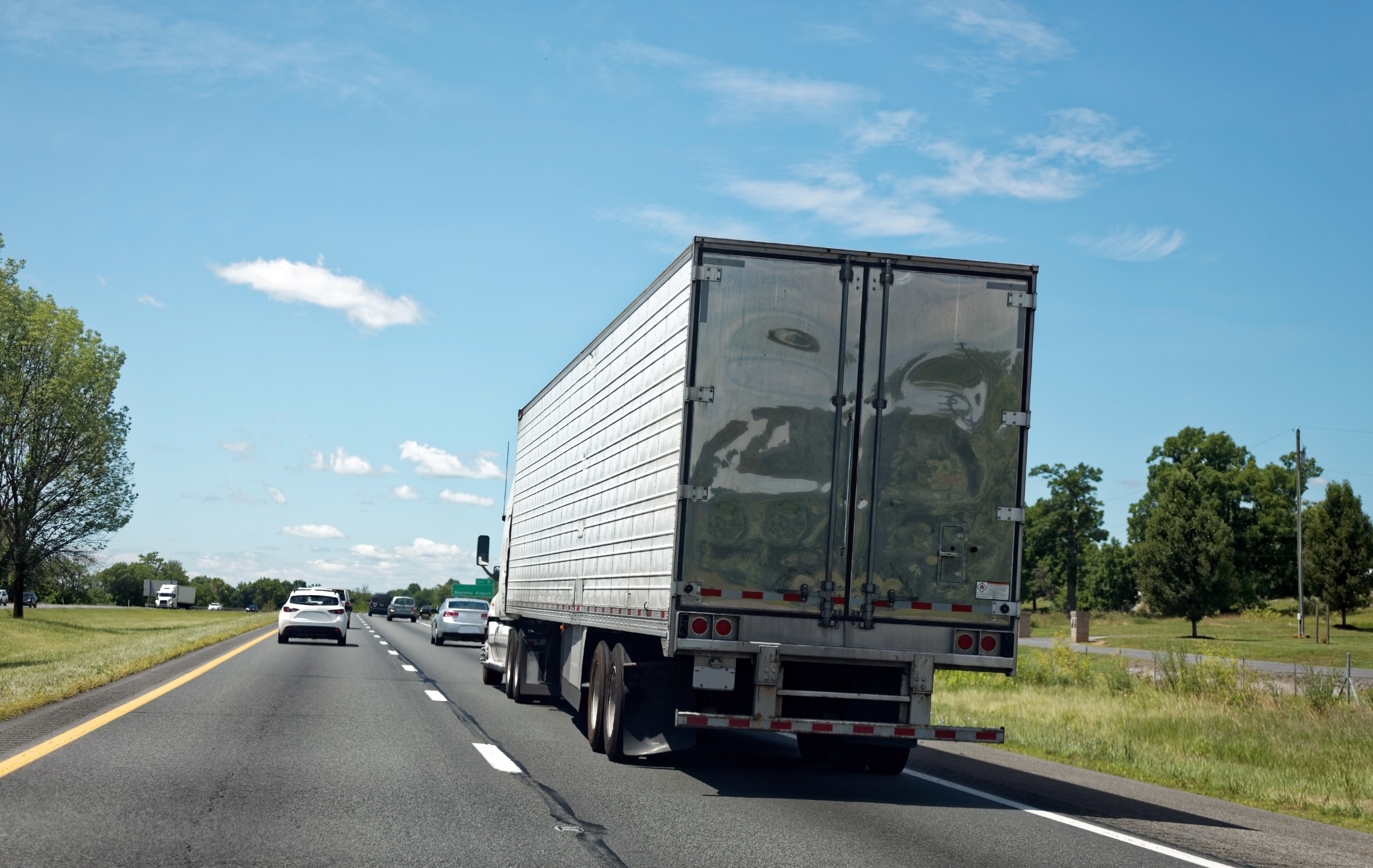Semi-truck driving on a multi-lane highway with clear blue sky and green landscape