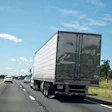 Semi-truck driving on a multi-lane highway with clear blue sky and green landscape