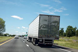 Semi-truck driving on a multi-lane highway with clear blue sky and green landscape