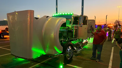 Customized green semi-truck with white cylindrical tank trailer illuminated by green LED lights at a truck show at dusk