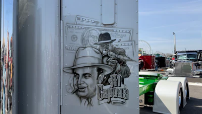 Al Capone themed street art mural on white trailer at outdoor car show with classic vehicles and Ferris wheel visible