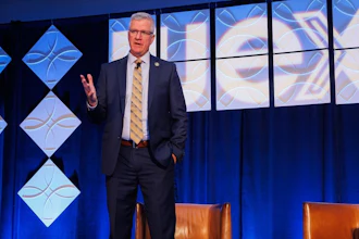 Professional speaker in business suit presenting on stage with blue geometric backdrop design