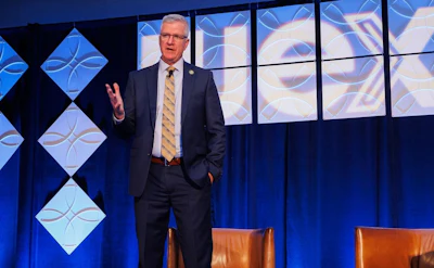 Professional speaker in business suit presenting on stage with blue geometric backdrop design