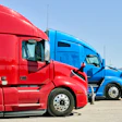 Red and blue semi-trucks parked side by side in an outdoor lot with clear sky