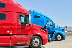 Red and blue semi-trucks parked side by side in an outdoor lot with clear sky
