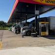 Love's Travel Stop facility with fuel pumps, parked trucks, and tanker trailer under covered canopy on clear day