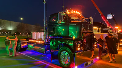 Illuminated custom semi-truck with neon green and blue lighting at nighttime outdoor event