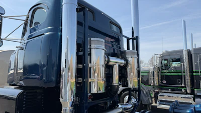 Fleet of dark blue and green semi-trucks parked in a row with chrome details and clear sky background
