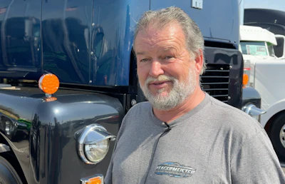 Man in TrafficMaster shirt standing in front of commercial trucks at a fleet yard