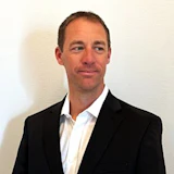 Professional headshot of a man in a black blazer and white shirt against a neutral background